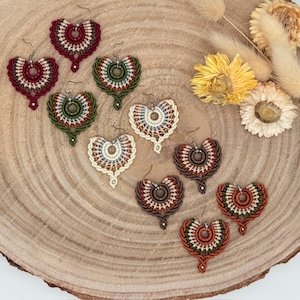 Könnte beinhalten: Ein Set aus sechs handgefertigten Makramee-Ohrringen in verschiedenen Farben, darunter Rot, Grün, Braun und Creme. Die Ohrringe sind herzförmig und weisen komplizierte Knotenmuster auf.