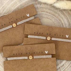 Könnte beinhalten: Drei Armbänder mit dem Text "Wear Me With" und einem Herzsymbol. Jedes Armband hat eine andere Buchstabenperle, B, I und G.