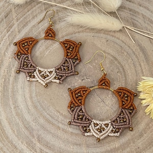 Könnte beinhalten: Ein Paar braune, beige und goldene Makramee-Ohrringe mit runder Form und Perlenmuster.