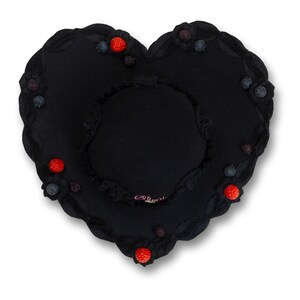May include: A black heart-shaped pillow with a smaller, circular pillow in the center. The edges are scalloped and adorned with red and blue berry-like embellishments. The pillow has a soft, plush appearance.