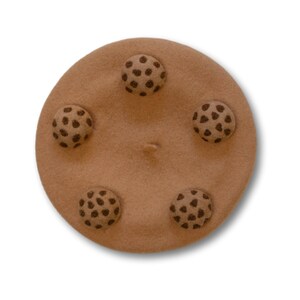 Op de afbeelding: Een bruine wollen baret met vijf bruine wollen knopen in de vorm van een koekje. De knopen hebben een bruin swirl-ontwerp.