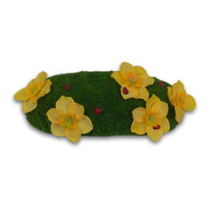 May include: An oval-shaped decorative piece featuring a green, grass-like surface adorned with yellow daffodils and small red ladybugs. The daffodils have a bright yellow color with a contrasting yellow center.