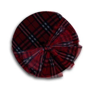 May include: A round, red and black plaid hat with a large bow. The hat features a classic tartan pattern in shades of red, black, and gray. The bow is made of a sheer, matching fabric.
