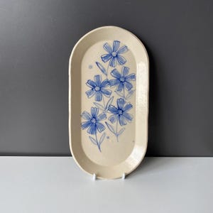 May include: A white oval ceramic serving tray with a blue floral design. The tray has a slightly raised rim and a smooth, glossy finish.