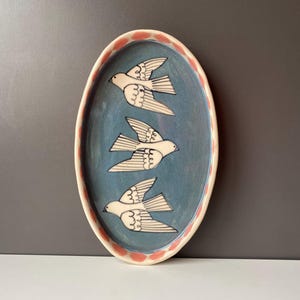 May include: A white ceramic mug with a black handle and the text "But First, Coffee" in a black, handwritten-style font. The mug is on a white surface.