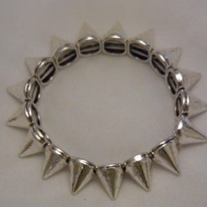 May include: A silver bracelet with a row of pointed spikes around the circumference.