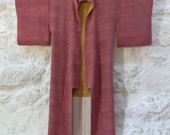 May include: A long, pink kimono with a yellow and white lining. The kimono is hanging on a wall.