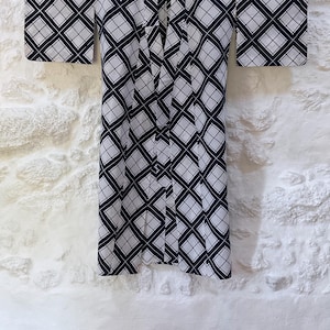 Puede incluir: Un kimono con estampado geométrico en blanco y negro con un diseño de rombos. El kimono está colgado en una pared blanca.