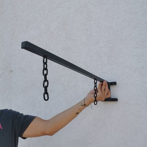 May include: A black metal sign holder with two chains hanging from it. The sign holder is mounted to a white wall.