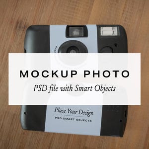 May include: A black and light blue disposable camera with a flash and lens. The camera has the text "MOCKUP PHOTO" and "PSD file with Smart Objects" on the front. The camera is on a wooden surface.