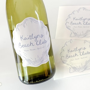 May include: A green wine bottle with a label that reads "Kaitlyn's Beach Club" in blue script. Two additional labels with the same design are also visible. The labels feature a seashell design and the text "Miami, Florida, April 2023".