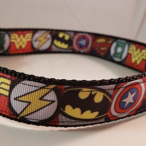 May include: A black dog collar with a colorful pattern of superhero logos, including Wonder Woman, Superman, Batman, and The Flash.