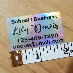 May include: A holographic business card with the name "Lily Davis", contact information, and the text "School / Business". The card is being measured with a tape measure, showing a length of approximately 5 cm.
