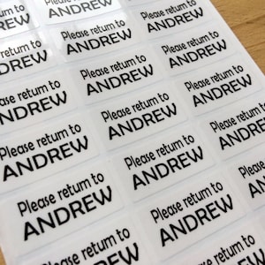 May include: A sheet of rectangular adhesive labels featuring the black printed text Please return to ANDREW. Each individual sticker is clear with a glossy finish, arranged in a grid pattern on a backing sheet for easy application and organization.