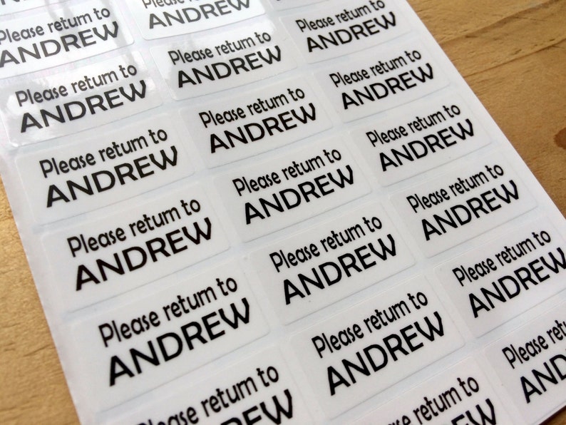 May include: A sheet of rectangular adhesive labels featuring the black printed text Please return to ANDREW. Each individual sticker is clear with a glossy finish, arranged in a grid pattern on a backing sheet for easy application and organization.