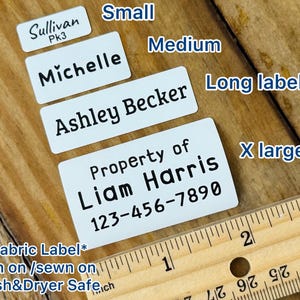 May include: White fabric labels with black text, including names and a phone number. Sizes range from small to extra-large. The text "*Fabric Label* Iron on / sewn on Wash&Dryer Safe.ch" is also visible.