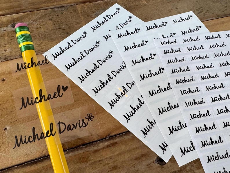 May include: Sheets of clear labels printed with the name "Michael" and "Michael Davis" in a cursive font. A yellow pencil with a pink eraser is in the foreground. The labels are for organizing and labeling items.