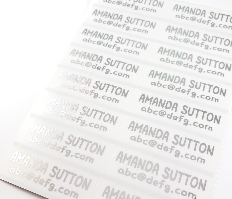 May include: A sheet of clear labels printed with the name "AMANDA SUTTON" and the email address "abc@defg.com" in a silver font. The labels are arranged in rows and columns, ready for use.