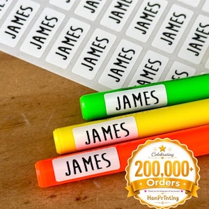 May include: A sheet of rectangular white adhesive labels with the name JAMES printed in black capital letters. Three of these labels are applied to bright green, yellow, and orange markers. A gold circular badge displays Celebrating 200,000+ Orders.