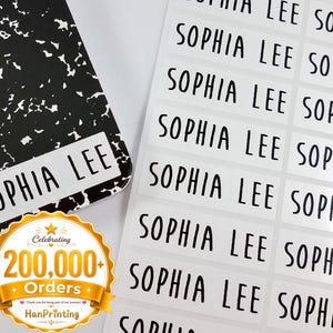 Peut inclure: Un carnet à motif marbré noir et blanc avec une étiquette rectangulaire blanche portant l'inscription SOPHIA LEE, accompagné d'une feuille d'étiquettes adhésives rectangulaires blanches, chacune imprimée du nom SOPHIA LEE en lettres capitales noires.