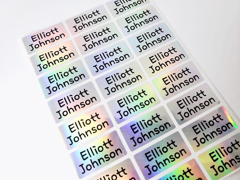 May include: A sheet of rectangular adhesive labels featuring a holographic finish that shifts in color. Each individual sticker is printed with the name Elliott Johnson in a bold, black, sans-serif font, arranged in a grid pattern on the sheet.