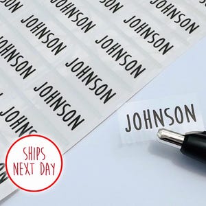 May include: A sheet of rectangular adhesive labels featuring the name JOHNSON printed in a bold black sans-serif font. One individual label is partially peeled away from the backing, positioned next to a black and silver ballpoint pen.