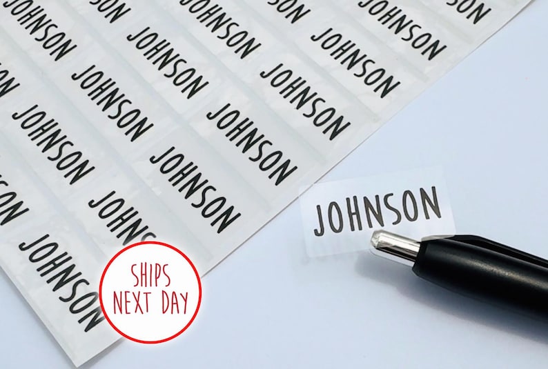 May include: A sheet of rectangular adhesive labels featuring the name JOHNSON printed in a bold black sans-serif font. One individual label is partially peeled away from the backing, positioned next to a black and silver ballpoint pen.
