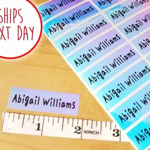 May include: A sheet of iridescent name labels with the name "Abigail Williams" printed in black. A single label and a measuring tape are also visible. The text "SHIPS NEXT DAY" is in a red circle.