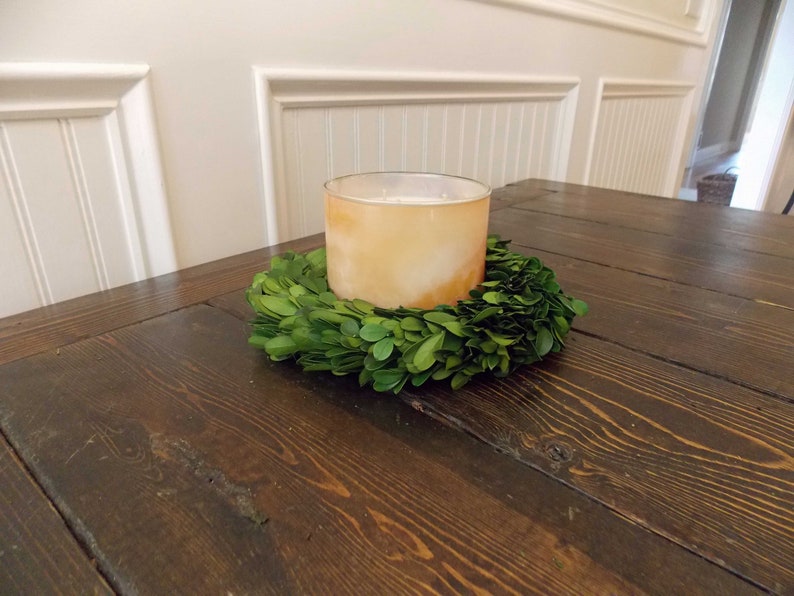 May include: A brown wooden table with a green boxwood wreath and a clear glass candle holder with a white candle inside.