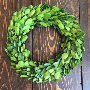 May include: A green boxwood wreath with a natural, rustic look. The wreath is made of small, green leaves and is perfect for adding a touch of greenery to your home decor.