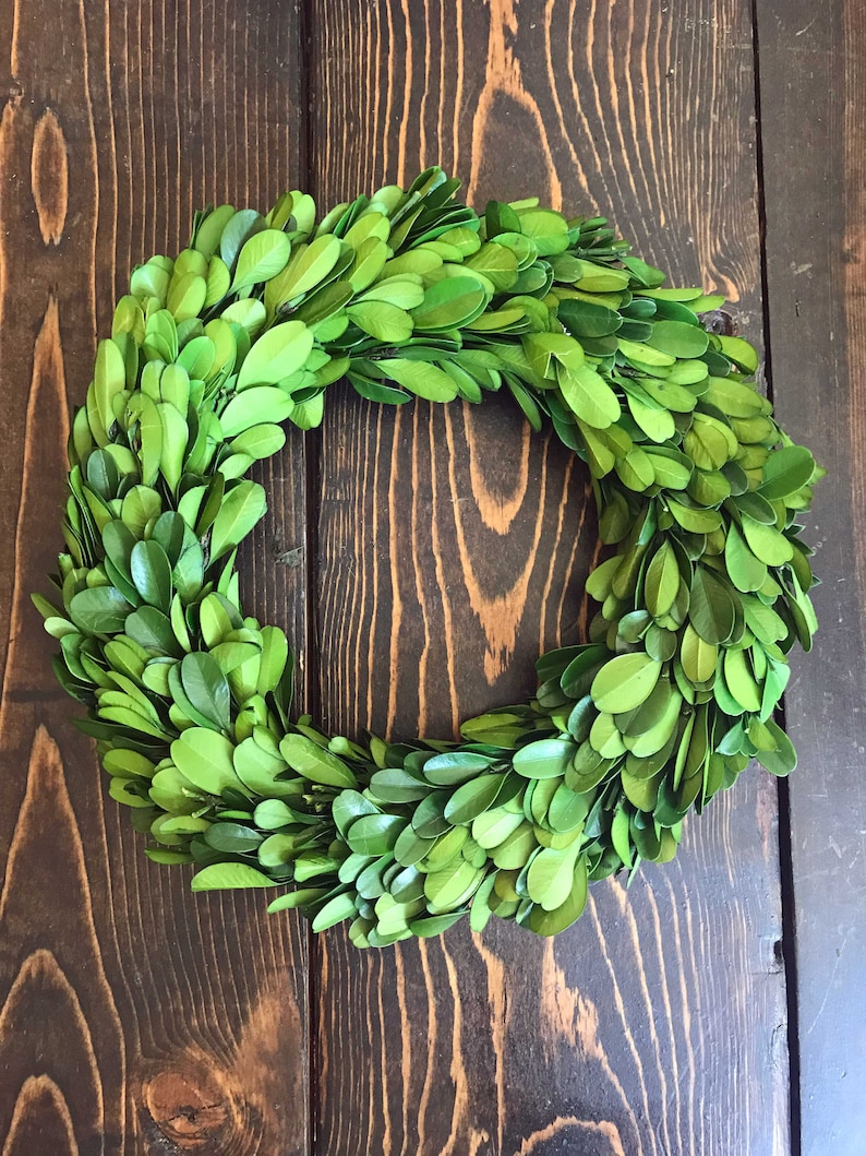 May include: A green boxwood wreath with a natural, rustic look. The wreath is made of small, green leaves and is perfect for adding a touch of greenery to your home decor.