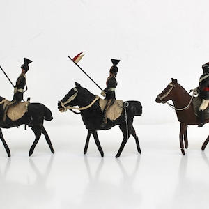 May include: Three toy soldiers on horseback, each holding a spear with a red and white flag. The soldiers are wearing black uniforms and black hats. The horses are black and brown.