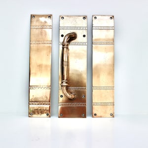 May include: Three brass door plates with a decorative design. The centre plate has a brass door handle.