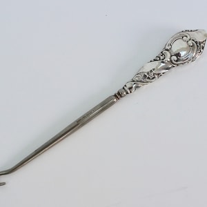 May include: A silver shoe horn with an ornate handle and a hook at the end.