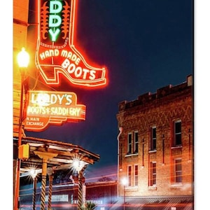 May include: A neon sign for "Leddy's Boots & Saddlery" with a red boot shape and the words "Hand Made Boots" in green. The sign is lit up at night and there is a building behind it.