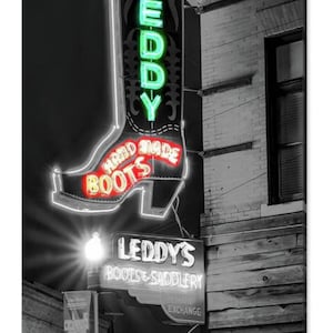 May include: Black and white photo of a storefront with a neon sign shaped like a cowboy boot. The sign reads "Leddy's Boots & Saddlery" and "Hand Made Boots".
