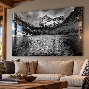 May include: A large rectangular wall art print featuring a black and white landscape photograph of the Maroon Bells mountains reflected in a calm lake, with snow-capped peaks, dense forest slopes, and rippled water surface textures.