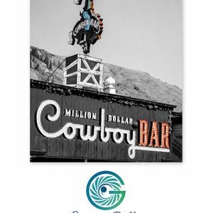 May include: A black and white photograph of the Million Dollar Cowboy Bar sign. A colorful neon cowboy on a bucking horse sits atop the building. The sign features the text Million Dollar Cowboy Bar in large, illuminated, vintage-style lettering.