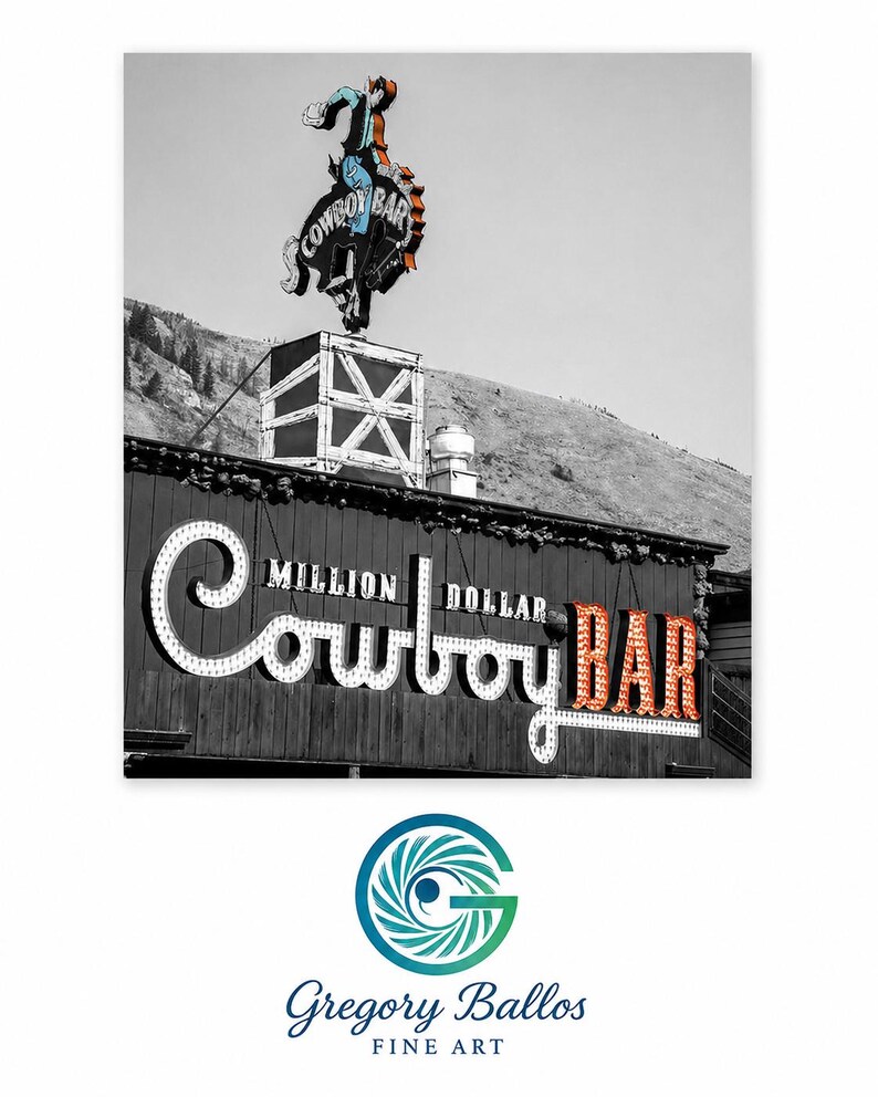 May include: A black and white photograph of the Million Dollar Cowboy Bar sign. A colorful neon cowboy on a bucking horse sits atop the building. The sign features the text Million Dollar Cowboy Bar in large, illuminated, vintage-style lettering.