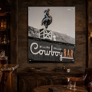 May include: A rectangular wall art print featuring a black and white photograph of the Million Dollar Cowboy Bar sign. The image displays a neon cowboy on a bucking horse atop a roof, with the text Million Dollar Cowboy Bar in illuminated letters.