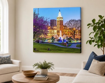 Può includere: Una stampa su tela quadrata che raffigura una scena notturna della fontana J.C. Nichols Memorial a Kansas City. L'immagine mostra un'alta torre in pietra, una fontana a più livelli con getti d'acqua illuminati e un albero con fiori viola.