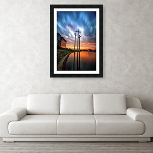 May include: Three wooden crosses stand tall against a dramatic sunset sky with clouds reflecting in a still body of water.