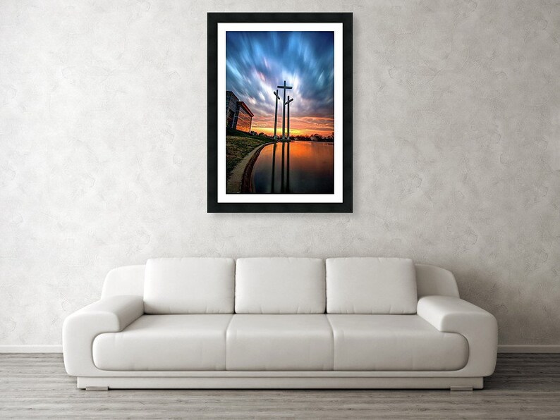 May include: Three wooden crosses stand tall against a dramatic sunset sky with clouds reflecting in a still body of water.
