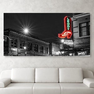 May include: A black and white photograph of a city street at night with a neon sign for "Leddy's Boot Shop" featuring a red boot. The sign is lit up and the street is empty.
