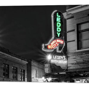 May include: Black and white photo of a neon sign for "Leddy's Hard Sole Boots" in the shape of a cowboy boot. The sign is lit up in green and red neon.