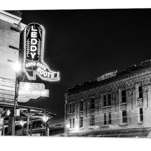 May include: Black and white photo of a storefront with a neon sign that reads "Leddy's Hand Made Boots". The sign is shaped like a cowboy boot. The storefront is located in a city at night.