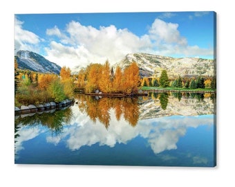 May include: A scenic landscape with a lake reflecting a mountain range with snow-capped peaks and a cloudy sky. The lake is surrounded by trees with yellow and orange leaves, creating a vibrant autumn scene.
