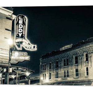May include: A black and white photo of a building with a neon sign that says "Leddy's Boots & Saddlery". The sign is shaped like a boot and has the words "Hand Made Boots" on it. The building is old and has a brick facade.
