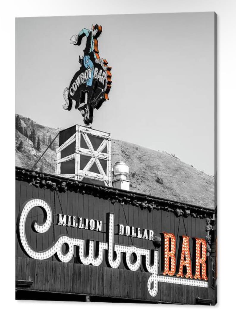 May include: A black and white photo of a building with a neon sign that says "Million Dollar Cowboy Bar". The sign is lit up in orange and white. A cowboy riding a bucking horse is on top of the building.
