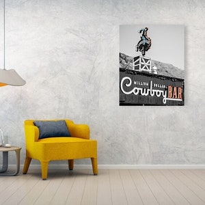 May include: Black and white photo of a sign for the "Million Dollar Cowboy Bar" in Wyoming. The sign features a cowboy riding a bucking bronco.